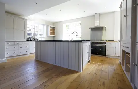 Large kitchen with grey painted cupboards, a panelled centre island, range cooker, leaded windows and oak floor