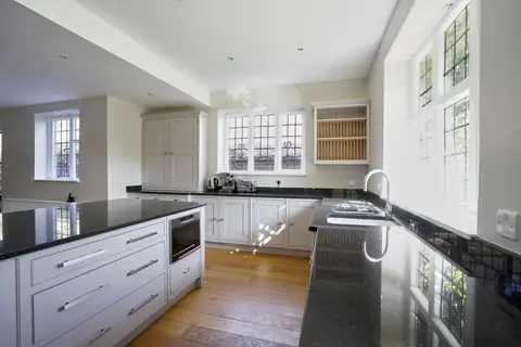 Grey painted kitchen island with drawers, a tall cupboard, plate rack and leaded windows with sunlight on the floor