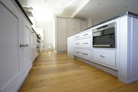 Low view along a grey painted island with drawers and a built-in oven towards tall grey cupboards