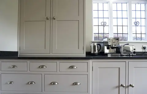 Grey painted drawers with cup handles and a two-door wall cupboard above a dark worktop with a coffee machine