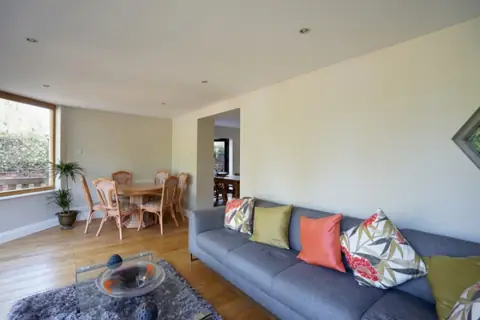 Family room with a grey sofa and patterned cushions, cream walls, a dining table and an opening to the kitchen