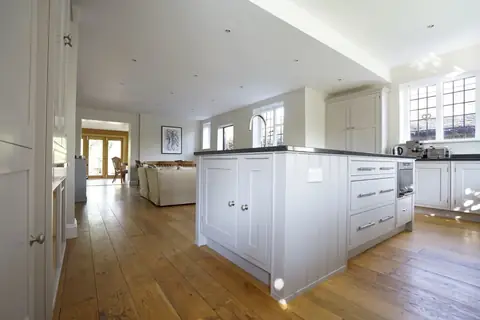 Grey painted kitchen island with drawers and a built-in oven, looking along oak boards to the family room