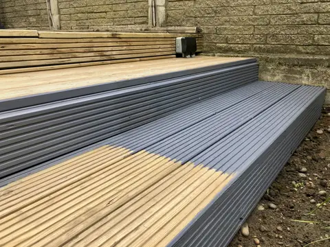 Garden decking steps with the lower boards stained grey and the upper boards still bare golden timber