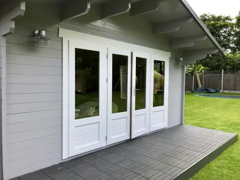Front of a light grey garden room with four white glazed doors, painted canopy brackets and two wall lights