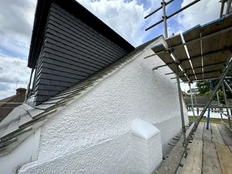 Freshly painted white pebbledash wall under a dark tile-hung dormer, seen from a scaffold platform