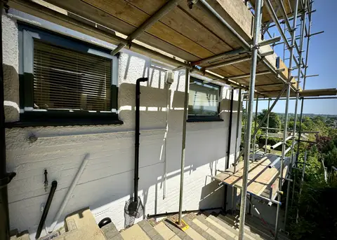 Side of a house painted white above garden steps, dark grey window frames, scaffold and a view down the hill