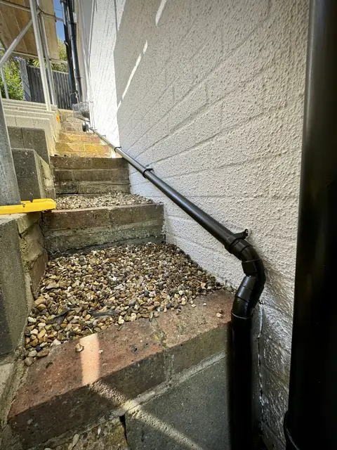 Narrow side passage with gravel steps beside a painted white textured wall and a black pipe