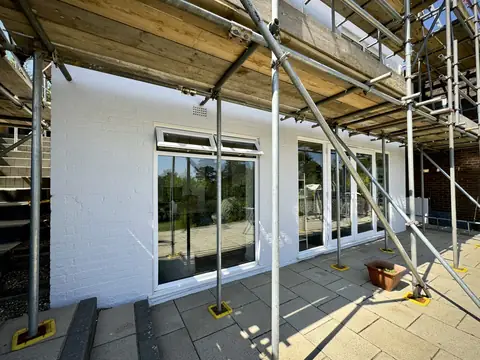 White painted brickwork and white patio doors on the ground floor at the back, under scaffold on a paved patio