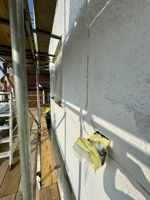 Window covered in polythene sheeting and yellow masking tape next to an unpainted pebbledash wall under scaffold
