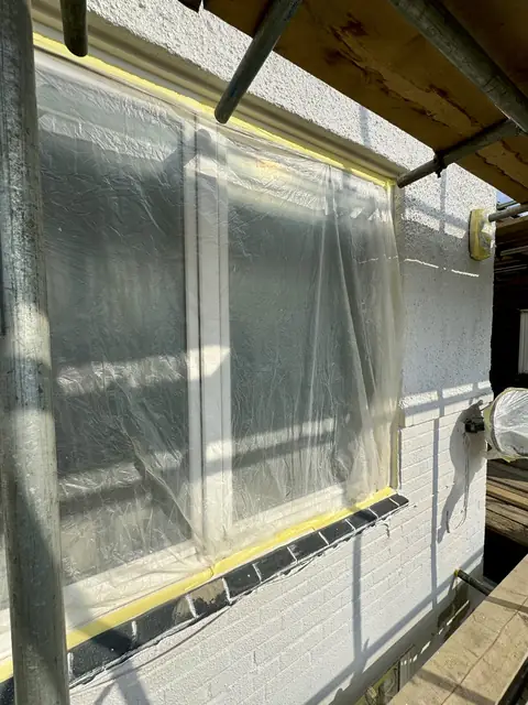 Large window sealed with polythene and yellow tape, the dark sill also taped off, under scaffold boards