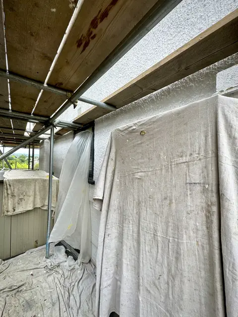 Dust sheets hung over a wall and railing and laid across a balcony floor under scaffold