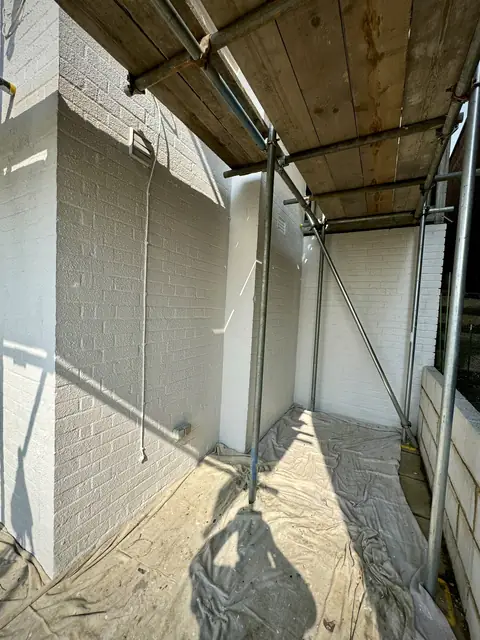 Corner of white painted brick walls under scaffold boards with dust sheets covering the ground