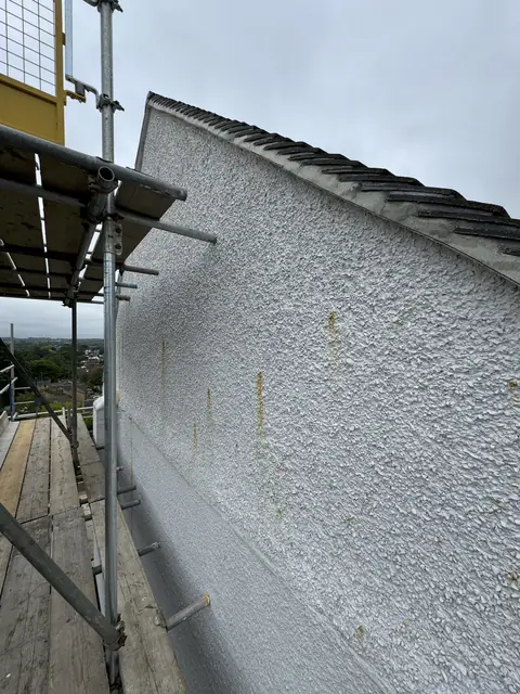 Old white pebbledash gable with orange-brown rust streaks running down from spots in the stones