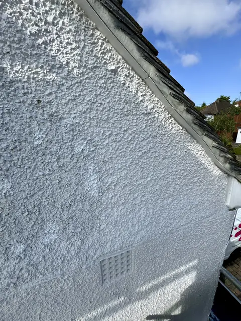 Painted white pebbledash gable rising to the roof tiles under a blue sky, with a wall vent near the bottom