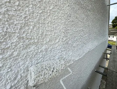 Pebbledash wall with a bright freshly painted band above the roller and a duller unpainted section beside it