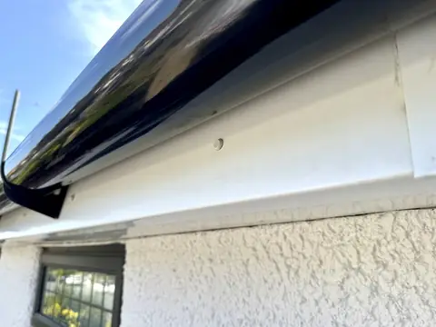 Clean bright white UPVC fascia under a glossy black gutter above white pebbledash and a dark window