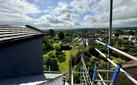 View from the top of the scaffold over long back gardens and rooftops, a slate-hung dormer on the left