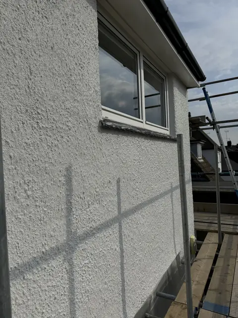 Concrete window sill part way through painting in anthracite grey, below a white window on white painted pebbledash