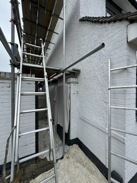 White painted brick and pebbledash meeting at a corner, with an anthracite grey band along the base and dust sheets below