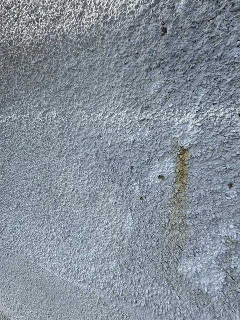 Close up of white painted pebbledash with small chipped-out holes and a brown rust streak in the texture