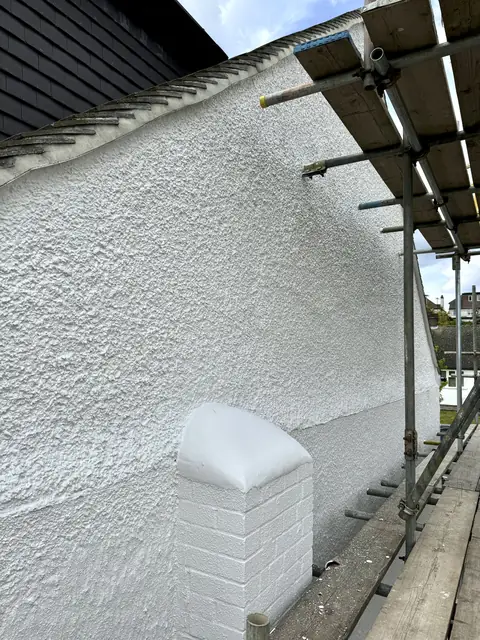 Upper side wall of white painted pebbledash with a rounded brick pier painted white, scaffold alongside