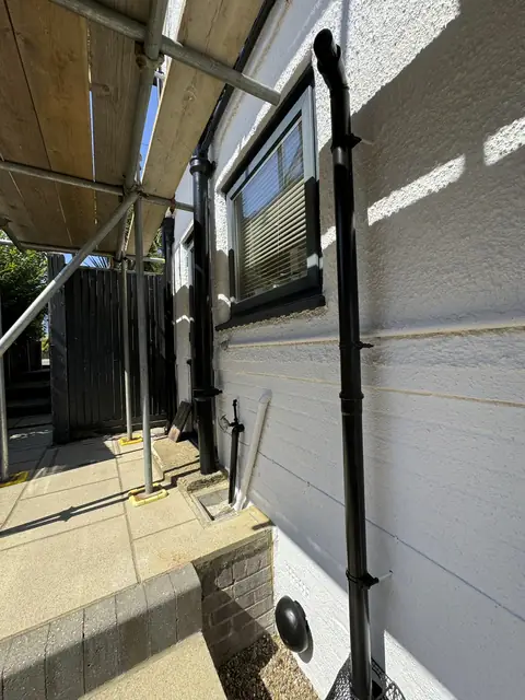 Side wall painted white with black downpipes and a dark framed window, scaffold over the passage