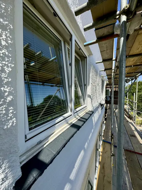 Concrete window sill painted anthracite grey beneath a white window, set in white painted pebbledash