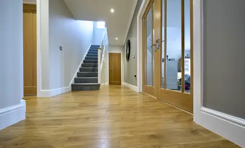 Low view along a hallway to carpeted stairs, with oak glazed doors on the right and white skirtings