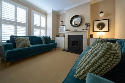 Redecorated lounge with warm neutral walls, white cornice, marble fireplace, two teal sofas and white window shutters