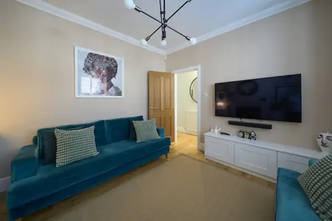 Lounge wall with framed portrait print above a teal sofa, oak door open to the hall and TV on the adjoining wall