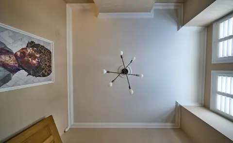 Looking straight up at a white lounge ceiling with cornice, ceiling rose and pendant light