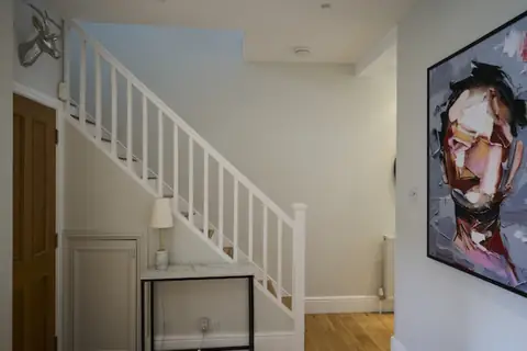 Open staircase with white spindles and newel post, oak door, console table and large painted portrait on the wall