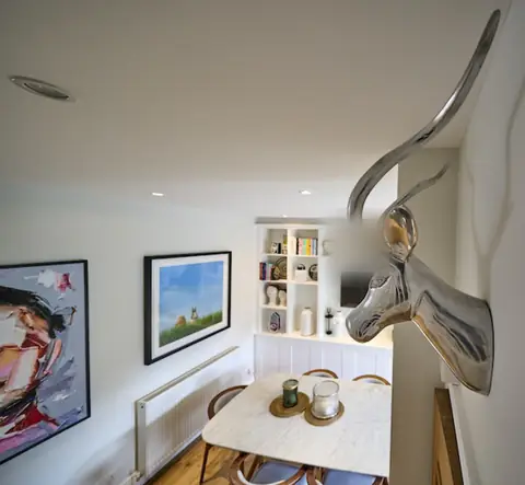 View down into a dining area with marble table, framed artwork, radiator and white shelving, silver antelope head on the wall