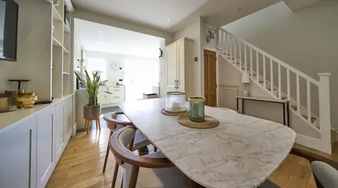 Marble dining table in an open-plan room, kitchen beyond and white staircase with oak door on the right