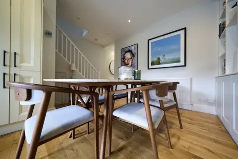 Low view of walnut dining chairs and marble table, framed prints on the wall and white staircase behind