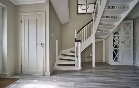 Hallway with greige walls, a white painted open-tread staircase, dark handrail and a matching panelled door