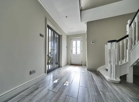 Hallway with a wood-effect floor, dark glazed double doors, a white staircase and the front door at the far end