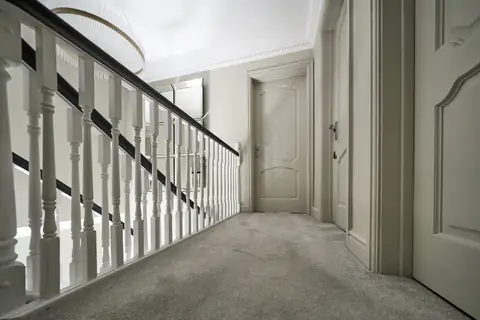 Landing balustrade with white spindles and a dark handrail leading to doors painted to match the walls