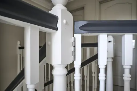 Close-up of a white newel post and spindles under dark painted handrails