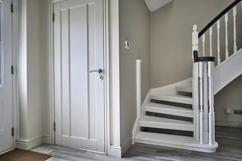 Pale panelled door and deep skirting beside the curved bottom steps of a white staircase with an Off Black handrail
