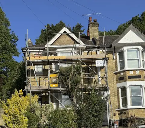 Victorian semi-detached house with yellow stock brick, scaffold up to the gable and front garden behind a low wall