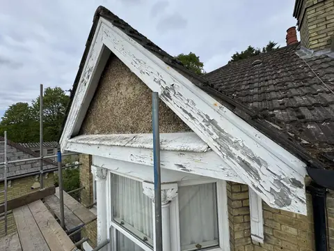 Gable of a Victorian house with peeling white paint on the barge boards and fascia above a bay window, seen from scaffold