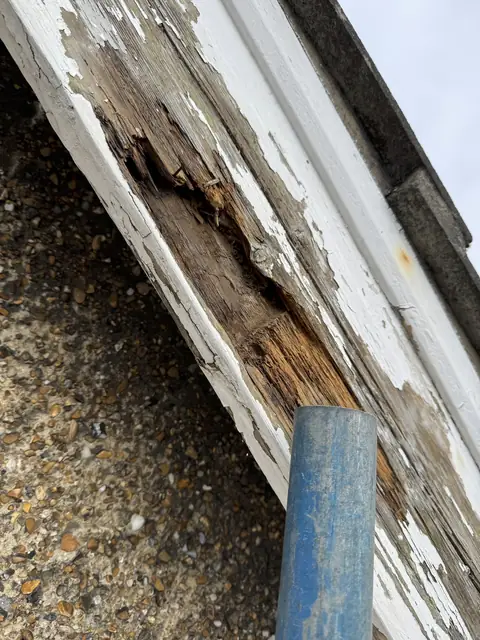Close-up of a gable barge board with a rotten, split section of timber under flaking white paint