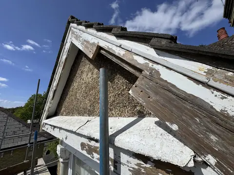 Gable barge board with a section of timber cut away, pebbledash behind and blue sky above