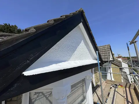 Repainted gable with black barge boards, white pebbledash and white soffit against a clear blue sky