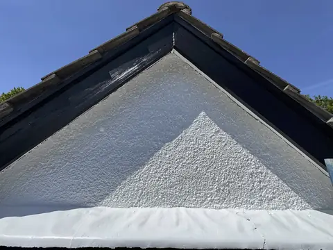 Looking up into the apex of a gable with black barge boards and white textured infill