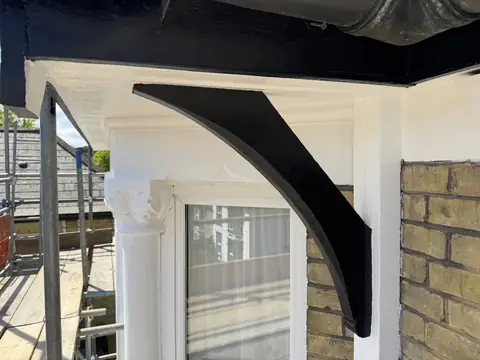Curved timber bracket painted black under a black fascia, with white soffit, bay window column and capital