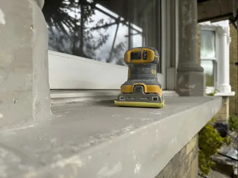 Yellow and black palm sander resting on a smooth, freshly filled grey stone window sill