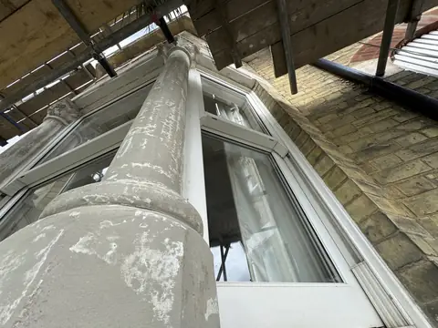 Looking up a bay window column patched in grey filler under scaffold boards