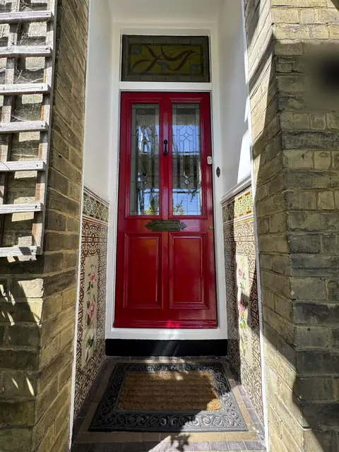 Glossy red front door with leaded glass panels and stained glass fanlight in a tiled Victorian porch